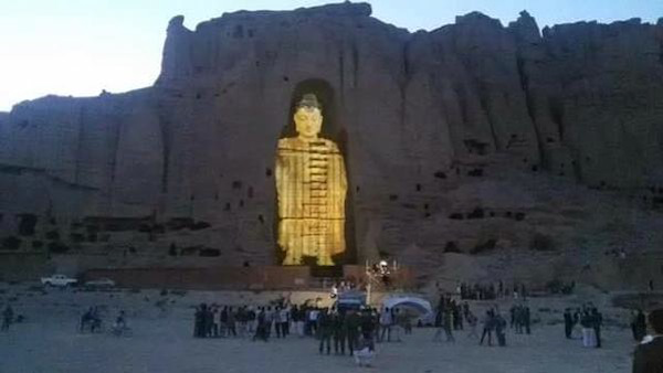 Image a projected Buddha glowing inside a 20 meter high carved inset in a cliff. People are milling about below.